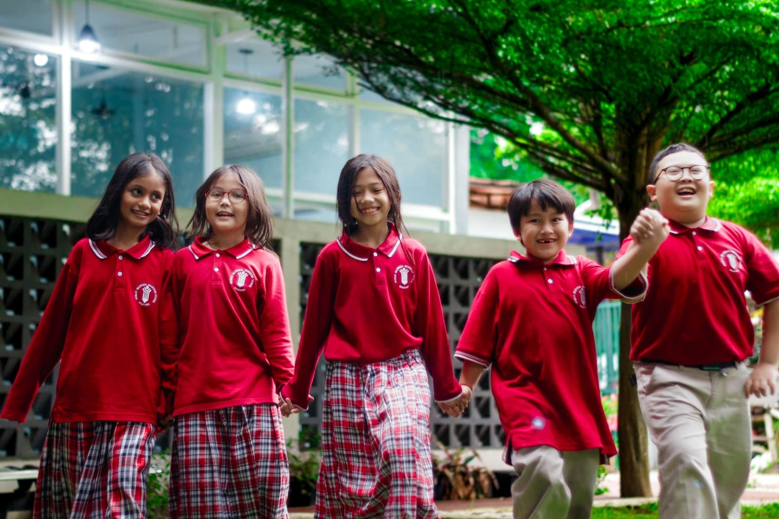 Primary students walking hand in hand under a campus tree