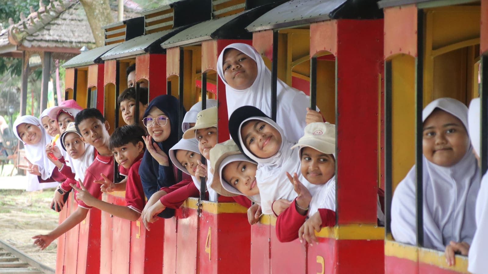 Students laughing from the windows of a red mini-train on a field trip