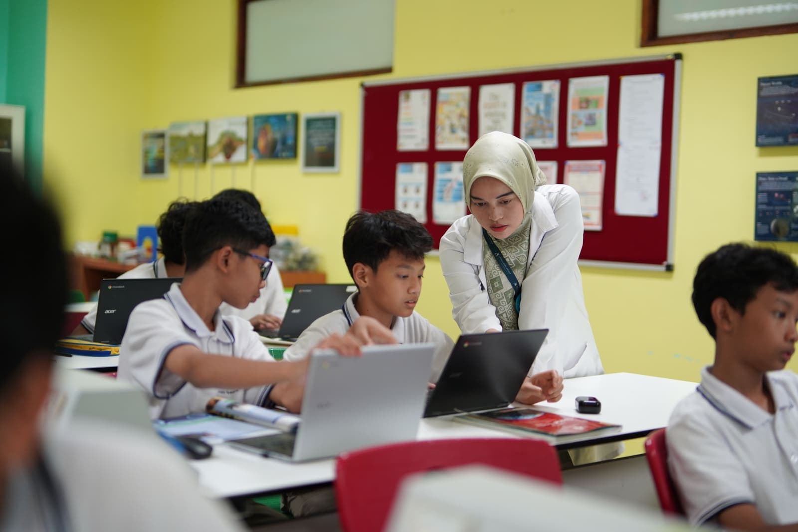 A teacher guiding students working on laptops