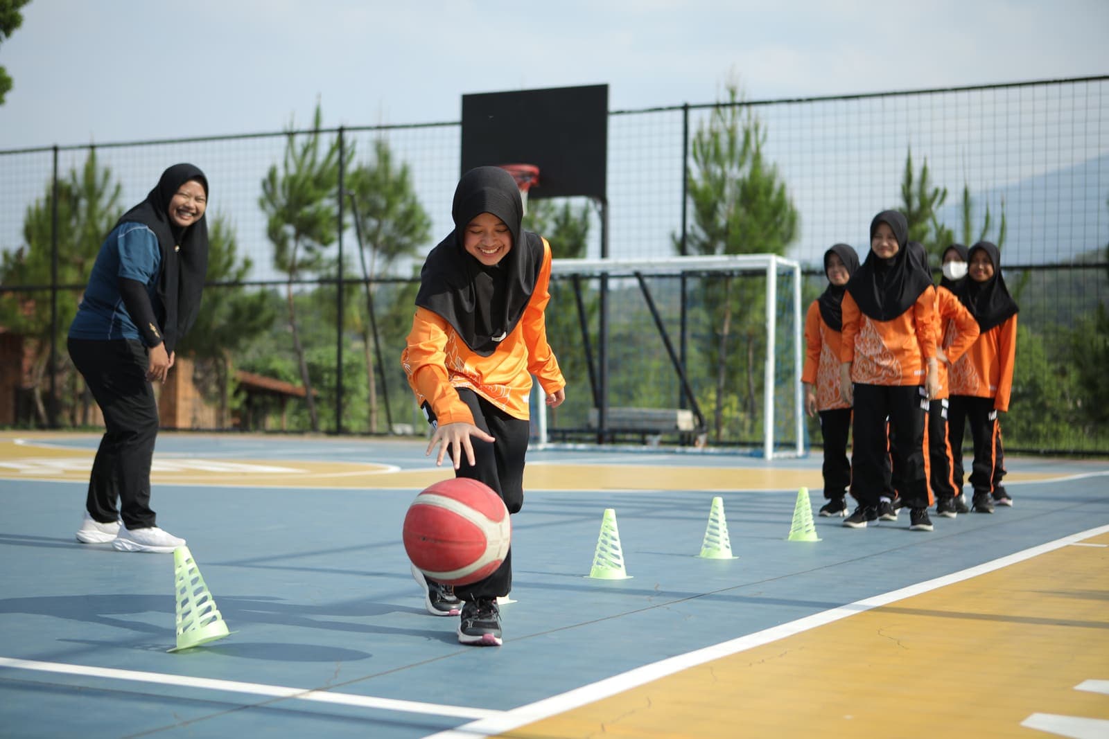 A beaming student dribbling a basketball through cones on an outdoor court